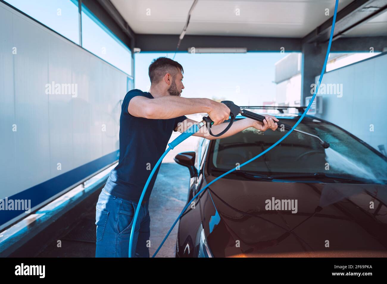 Young man washing car in self serve car wash. Cleaning car using high