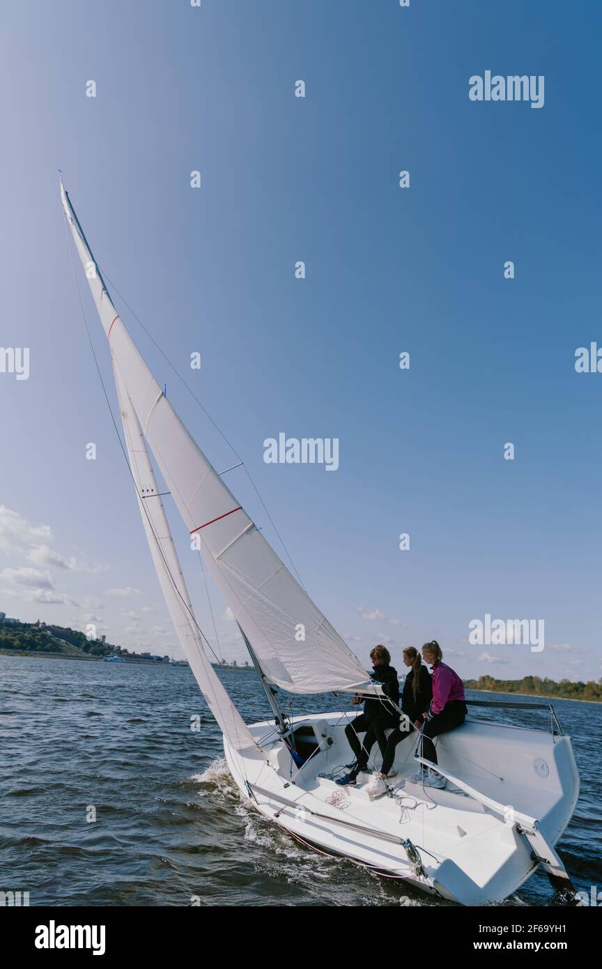A Beautiful White Racing Single Masted Yacht Is Sailing Against A Beautiful River Landscape With A Blue Sky A Man And Two Girls Are On Board Stock Photo Alamy