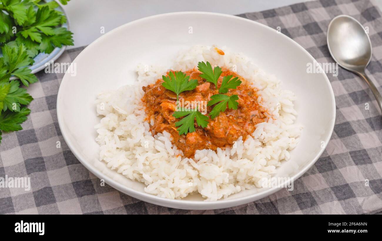 Rice with chicken meat cooked with paprika and sour cream, served with fresh parsley, close up on kitchen table Stock Photo