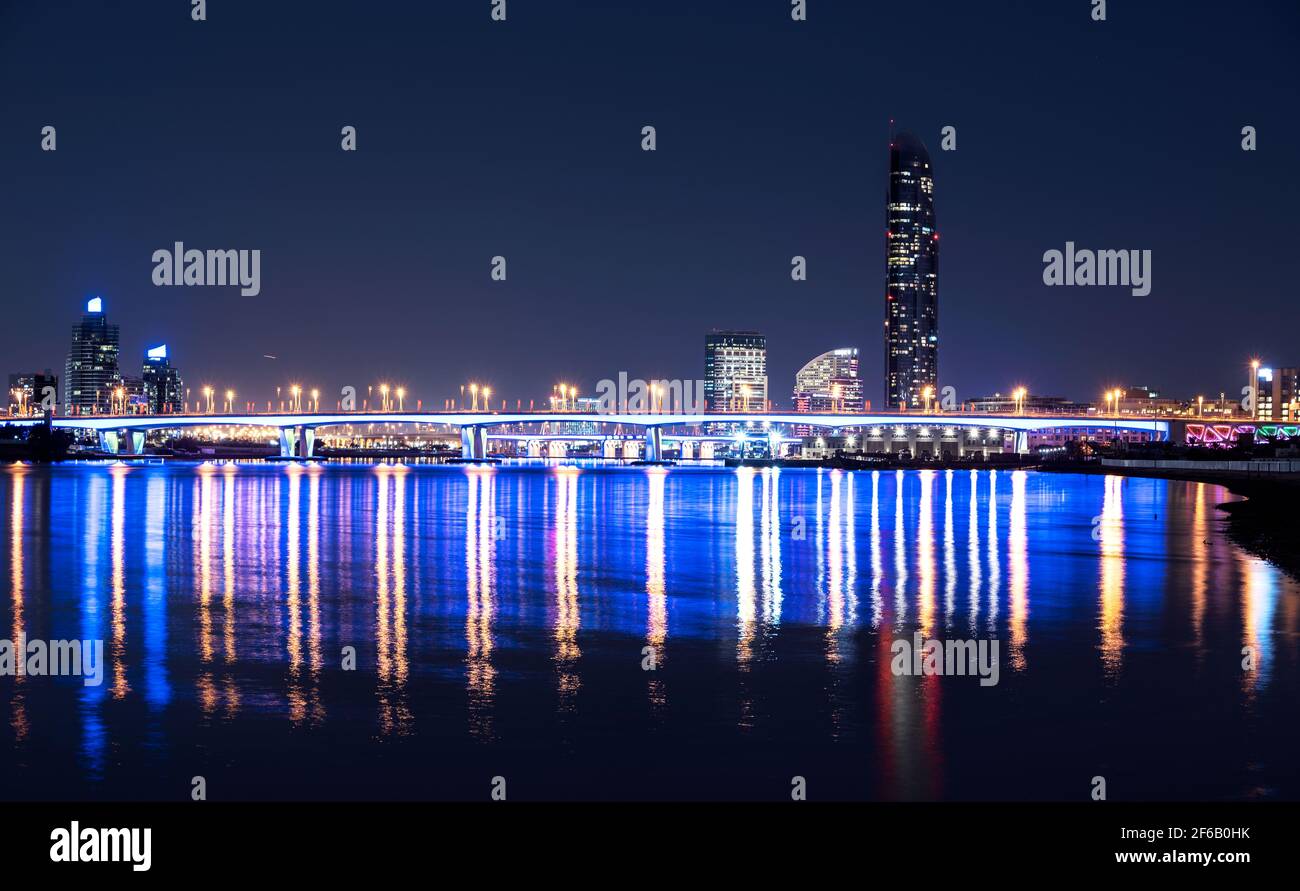 Beautiful night view of the illuminated Garhoud bridge across the water with reflections, surrounded by sky scrappers captured from Dubai Creek Park Stock Photo