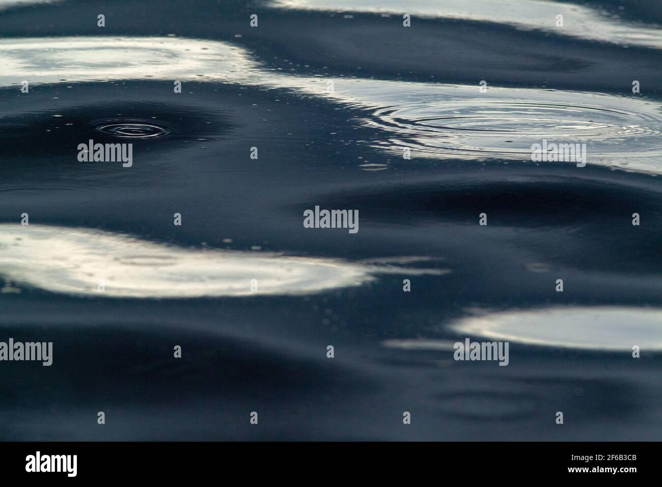 Patterns, shapes, created, formed, forming, evolving, from continuous, continuing, falling raindrops on a flowing river surface. Highlight, highlights Stock Photo