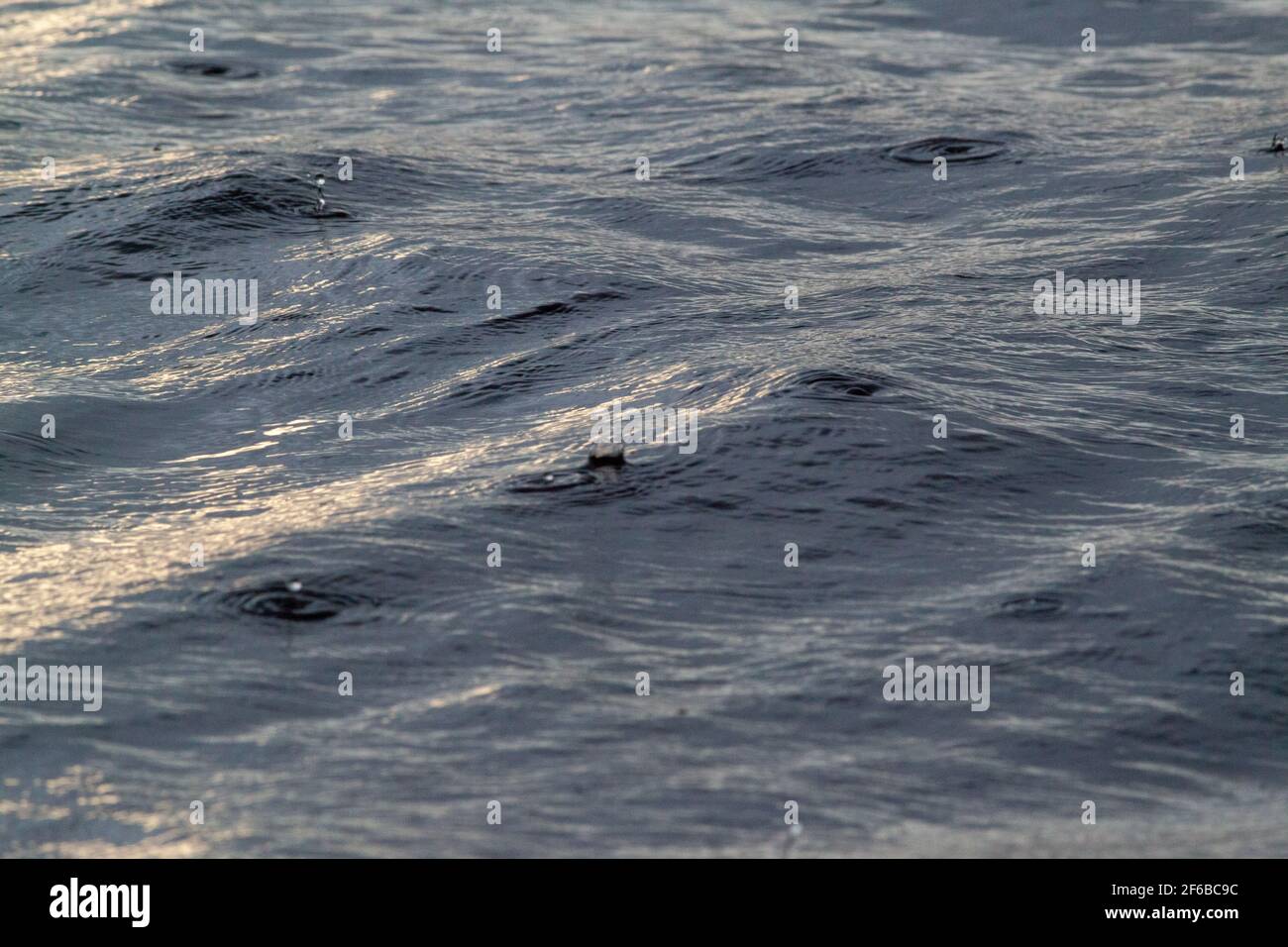 Patterns, shapes, created, formed, forming, evolving, from continuous, continuing, falling raindrops on a flowing river surface. Highlight, highlights Stock Photo
