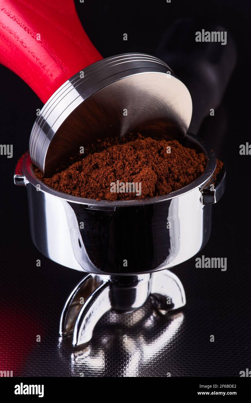 Barista accessories, portafilter with fresh ground coffee and tamper on shiny table bar, close-up view Stock Photo