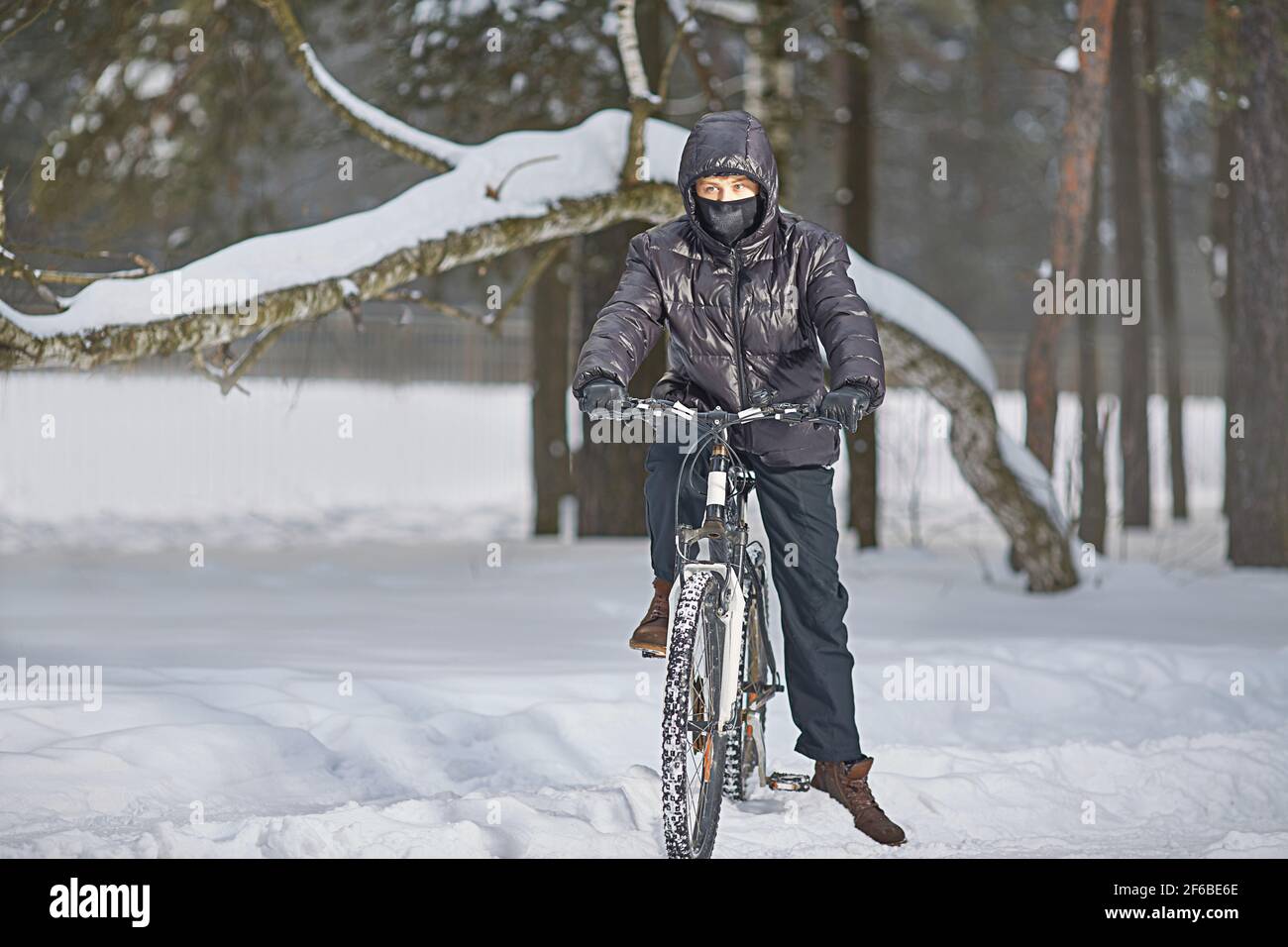 Active winter recreation. A teenager in a buff and black clothes rides a bike in winter. Stock Photo