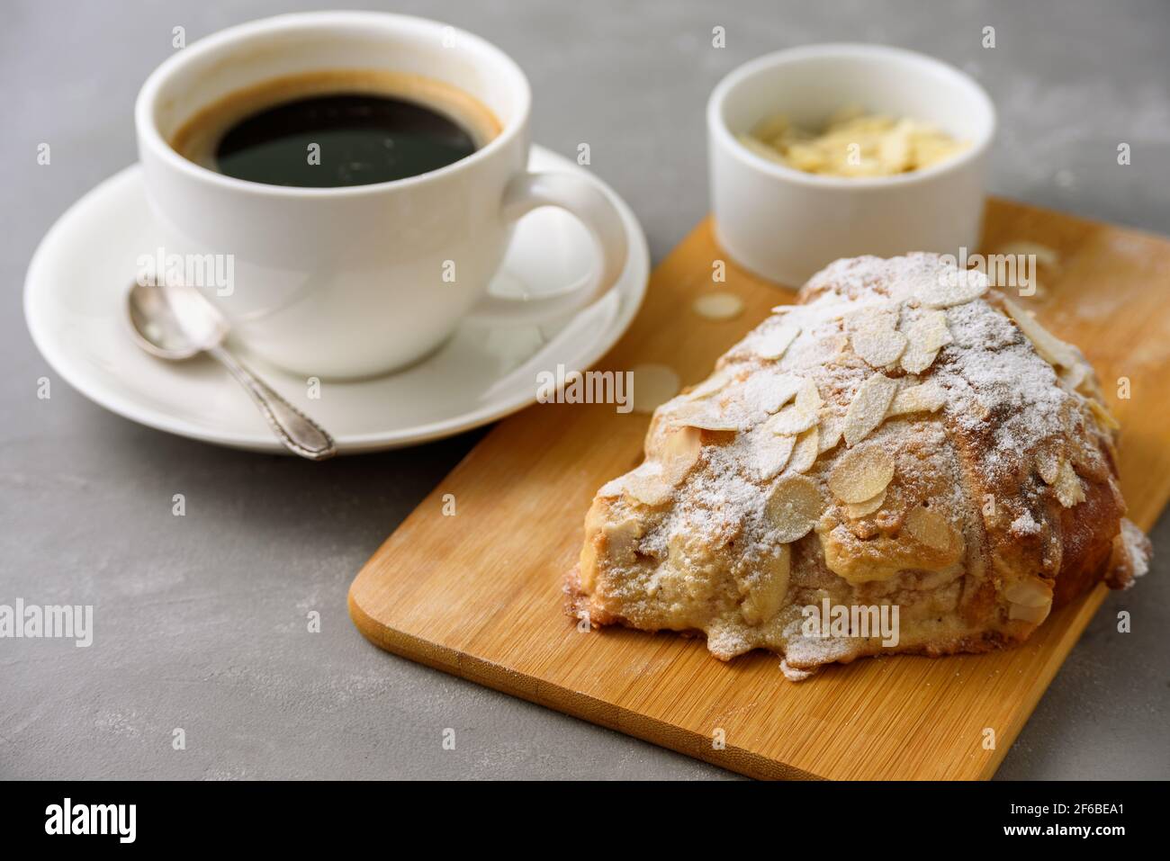 almond-croissant-on-wooden-board-with-black-coffee-on-concrete-grey