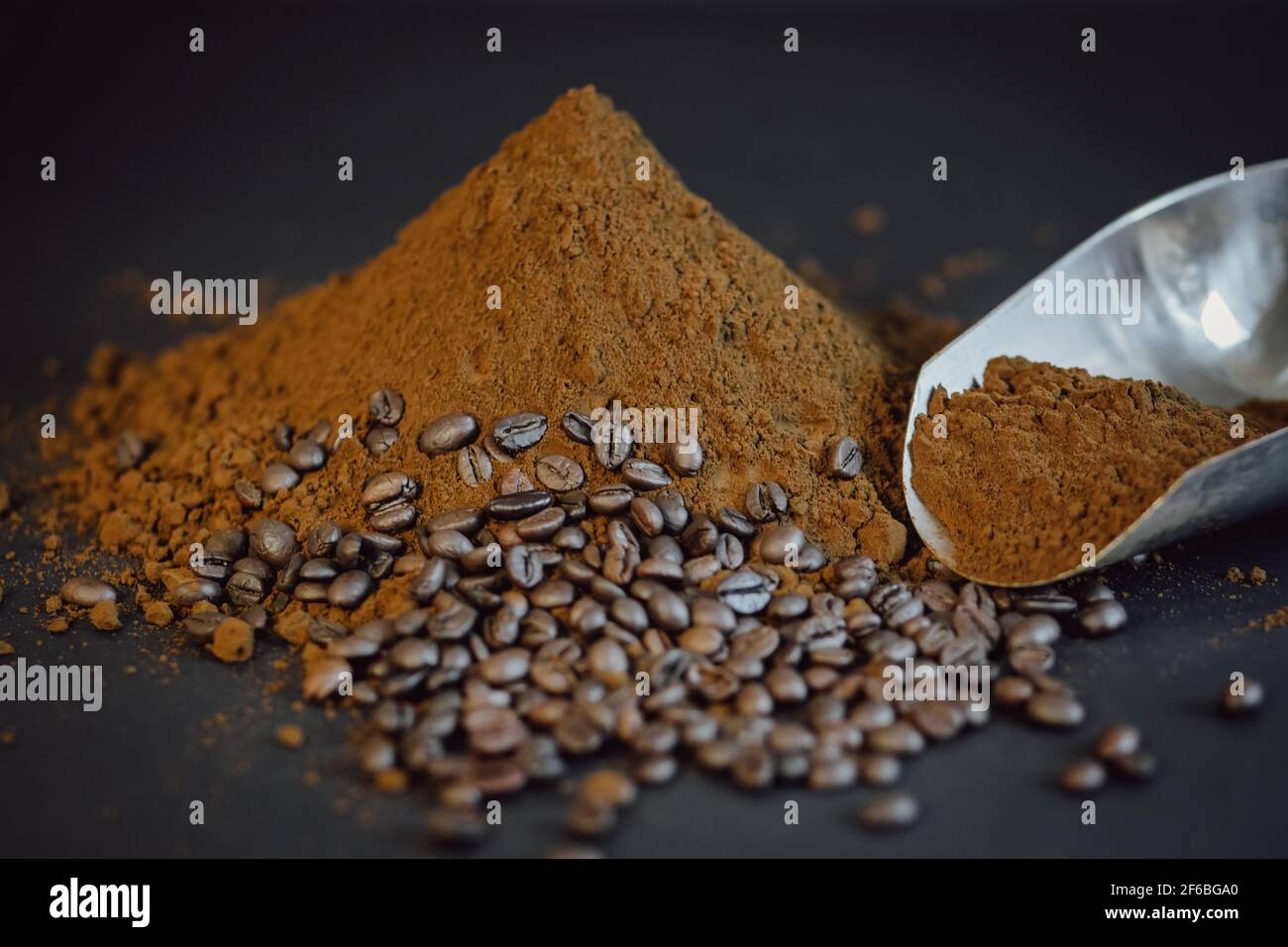 Ground coffee drips out of the scoop. Coffee powder and beans on black