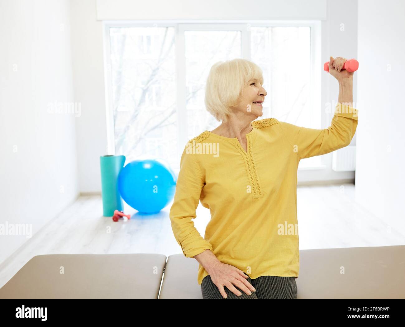 Senior patient while exercise treatment using dumbbells for strengthening arm muscles . Rehab at