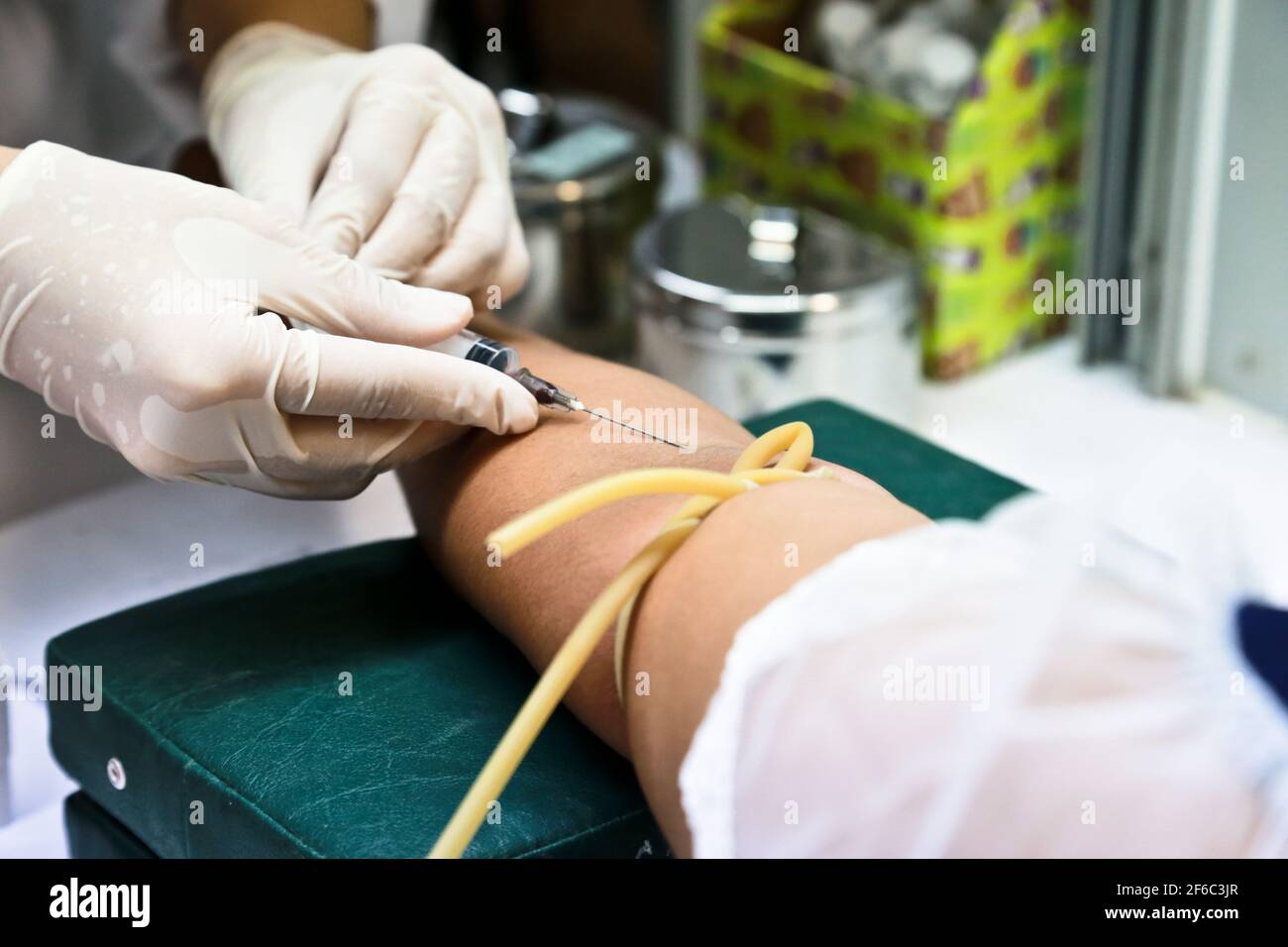 Doctor or nurse hands in medical white gloves using needle syringe drawing blood sample from patient arm in hospital. Stock Photo
