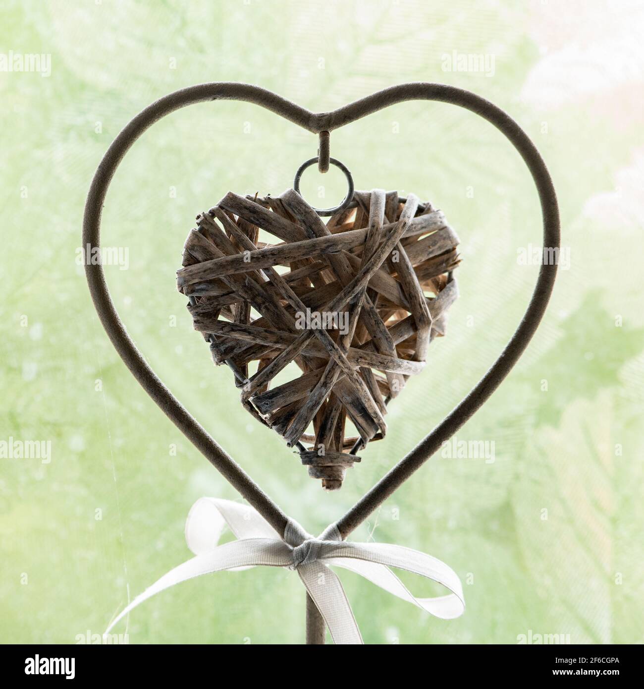 A wicker heart within a heart against frosted glass in front of a green background. Stock Photo