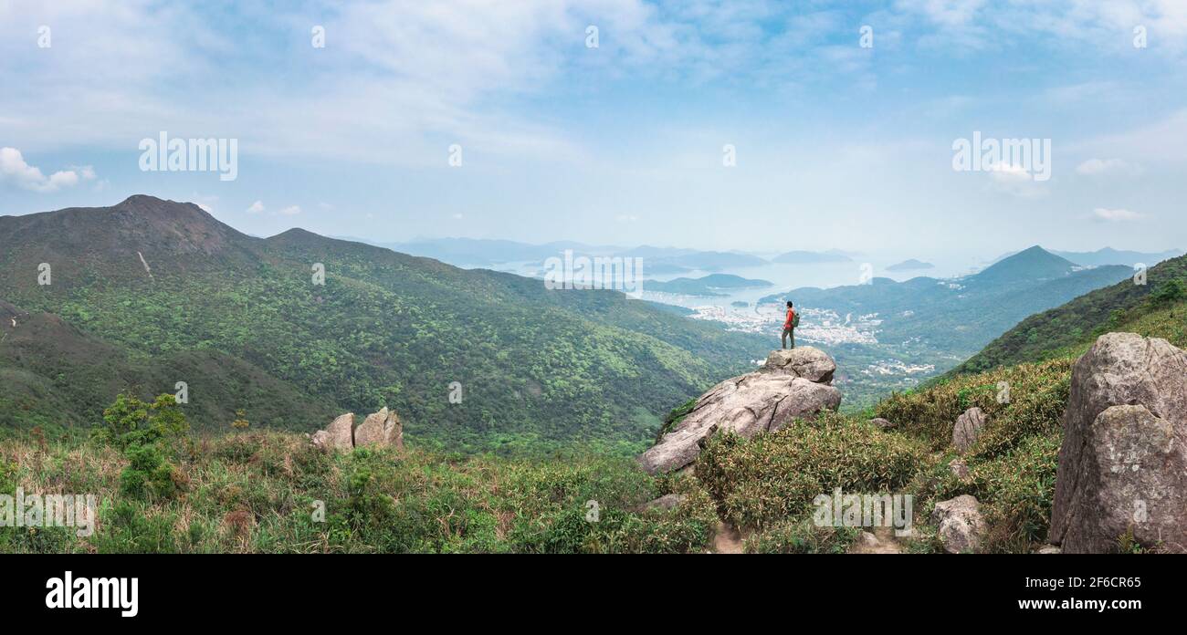 Hiking man standing on the rock, mountain peak. Sai Kung, Hong Kong, outdoor, daytime Stock Photo
