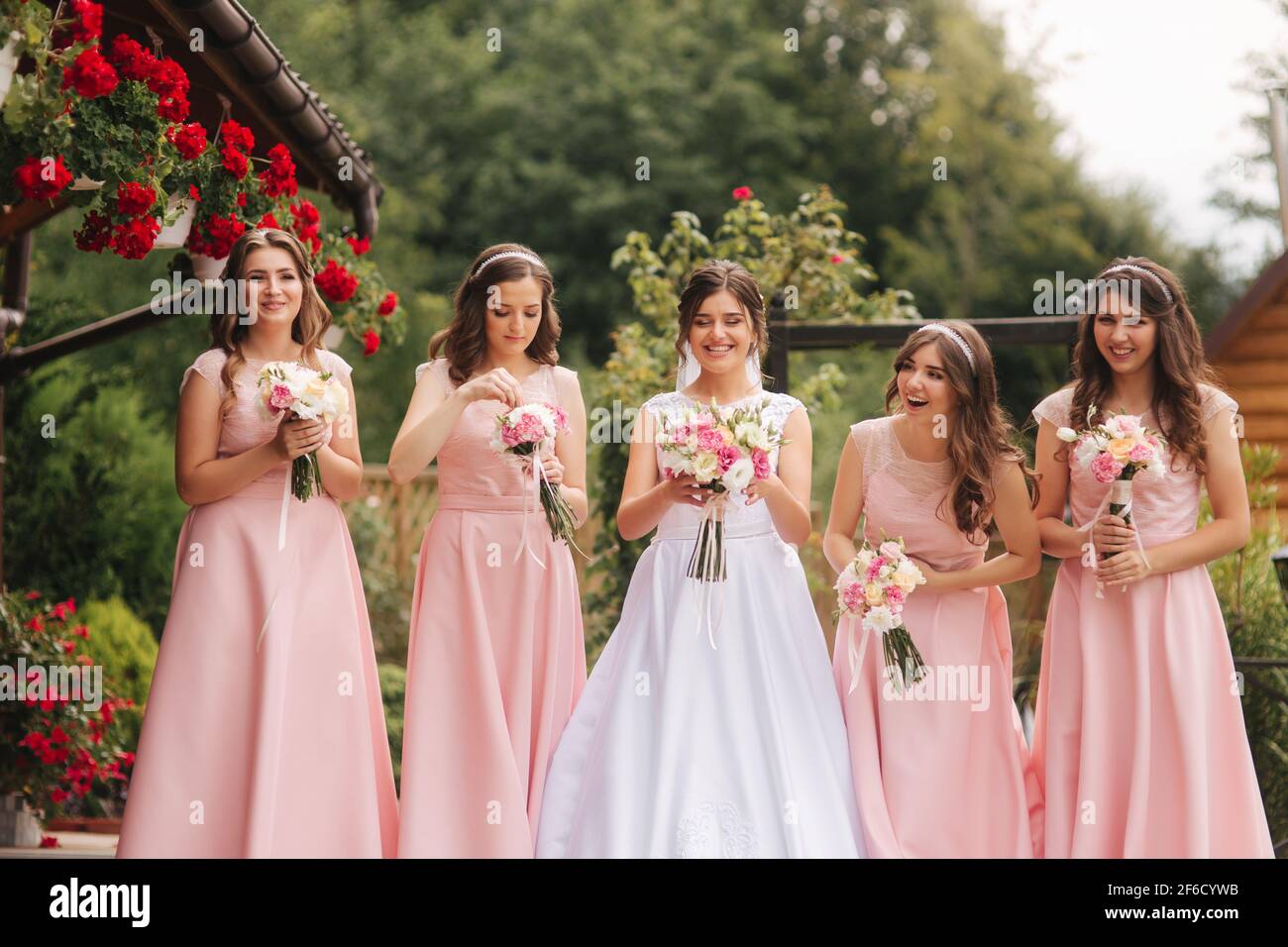 https://c8.alamy.com/comp/2F6CYWB/happy-bride-with-bridesmaid-hold-bouquets-and-have-fun-outside-beautiful-bridesmaid-in-same-dresses-stand-by-the-charming-bride-in-long-wedding-dress-2F6CYWB.jpg