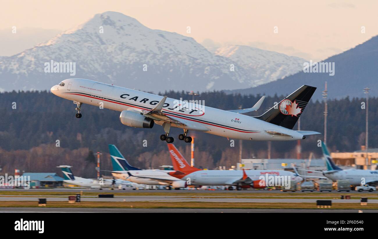 Richmond, British Columbia, Canada. 29th Mar, 2021. A Cargojet Boeing 757 air cargo jet (C-GTCJ) takes off at sunset from Vancouver International Airport, Richmond, B.C. on Monday, March 29, 2021. In the background WestJet and Sunwing Boeing 737 jets are seen parked at the airport's domestic terminal. Credit: Bayne Stanley/ZUMA Wire/Alamy Live News Stock Photo