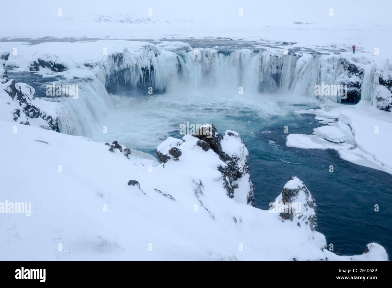 Goðafoss waterfall complex with a photographer near to the edge during winter conditions showing the 12 metre drop full of ice features on the  river Stock Photo