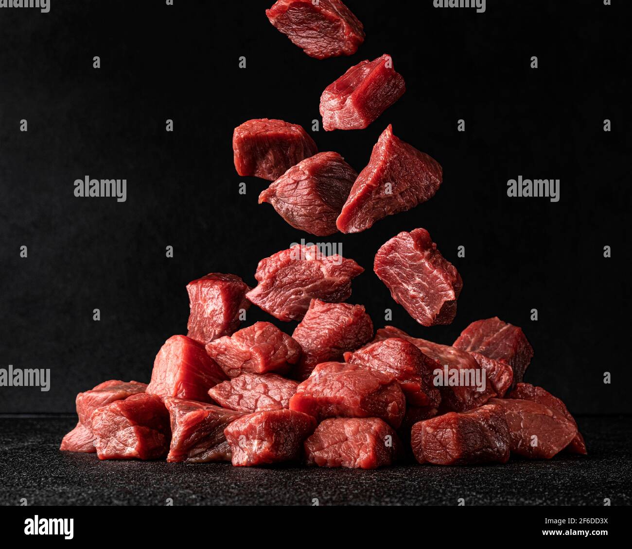 Cubes of raw beef falling over black background Stock Photo