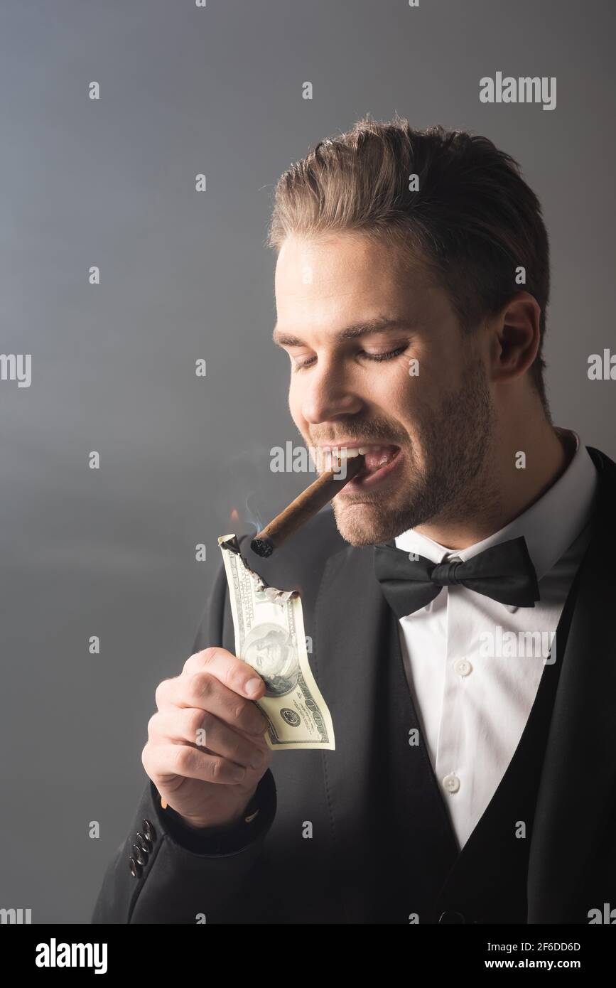 wealthy businessman lighting cigar with hundred dollar banknote on grey