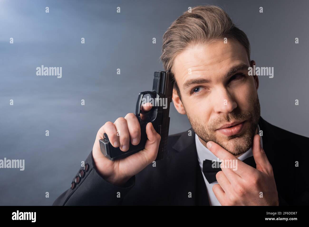 thoughtful businessman touching face while holding gun near head on grey background with smoke Stock Photo
