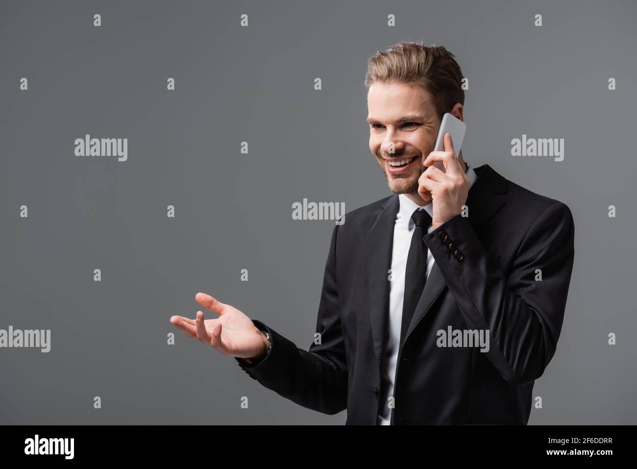 joyful manager pointing with hand while talking on cellphone isolated on grey Stock Photo