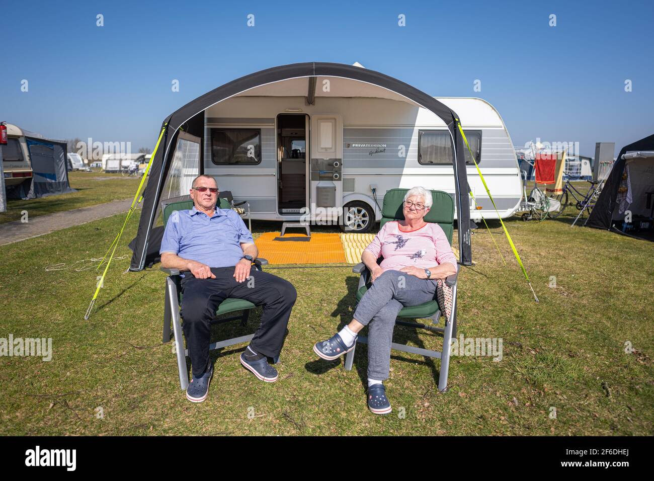 Hooksiel, Germany. 31st Mar, 2021. The permanent campers Karl-Heinz and  Anna from Herford are sitting in front of their caravan on the camping site  of Hooksiel, where they have planned their stay