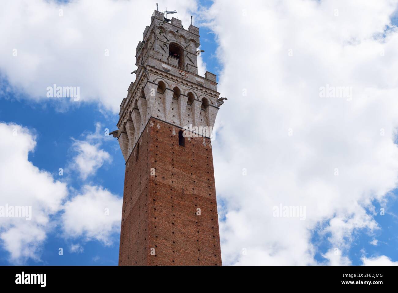 Detail of the Torre del Mangia 87 m. Tower of Mangia on blue sky with clouds. Siena, Italy Stock Photo