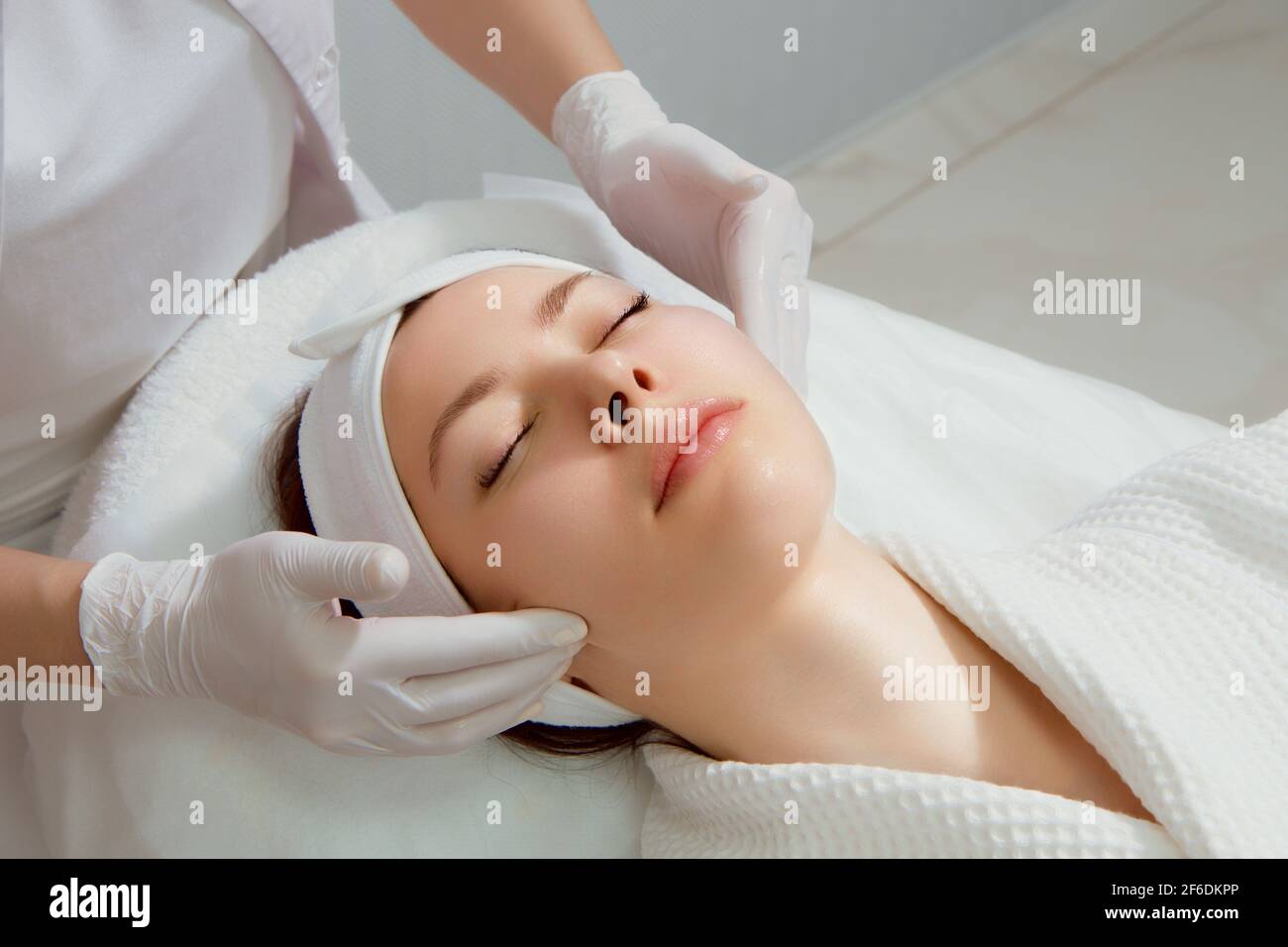 A young woman with perfect skin gets a facial massage at a cosmetology clinic Stock Photo