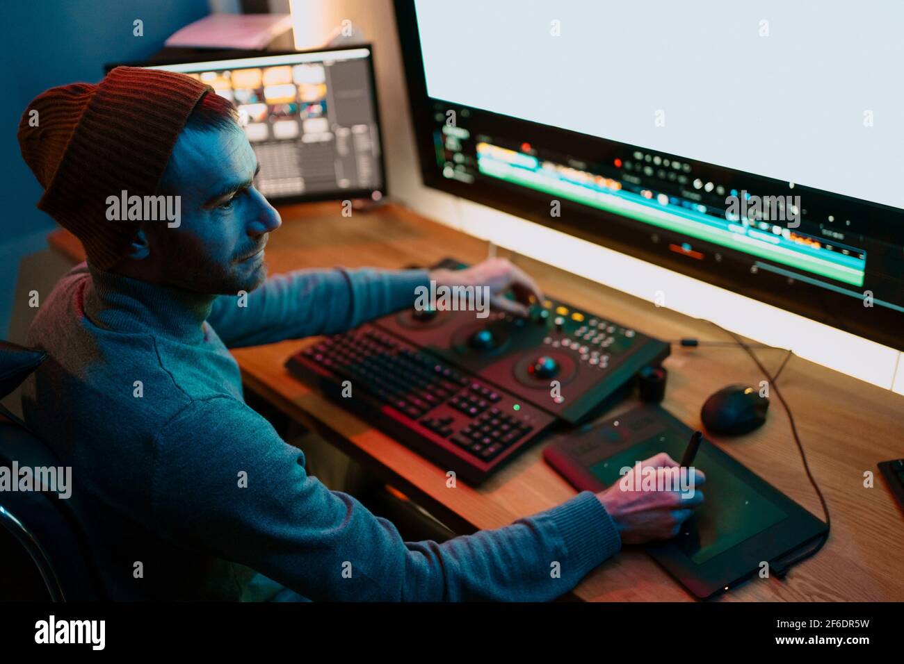 Attractive Male Video Editor Works with Footage or Video on His Personal Computer, he Works in Creative Office Studio or home. Neon lights Stock Photo