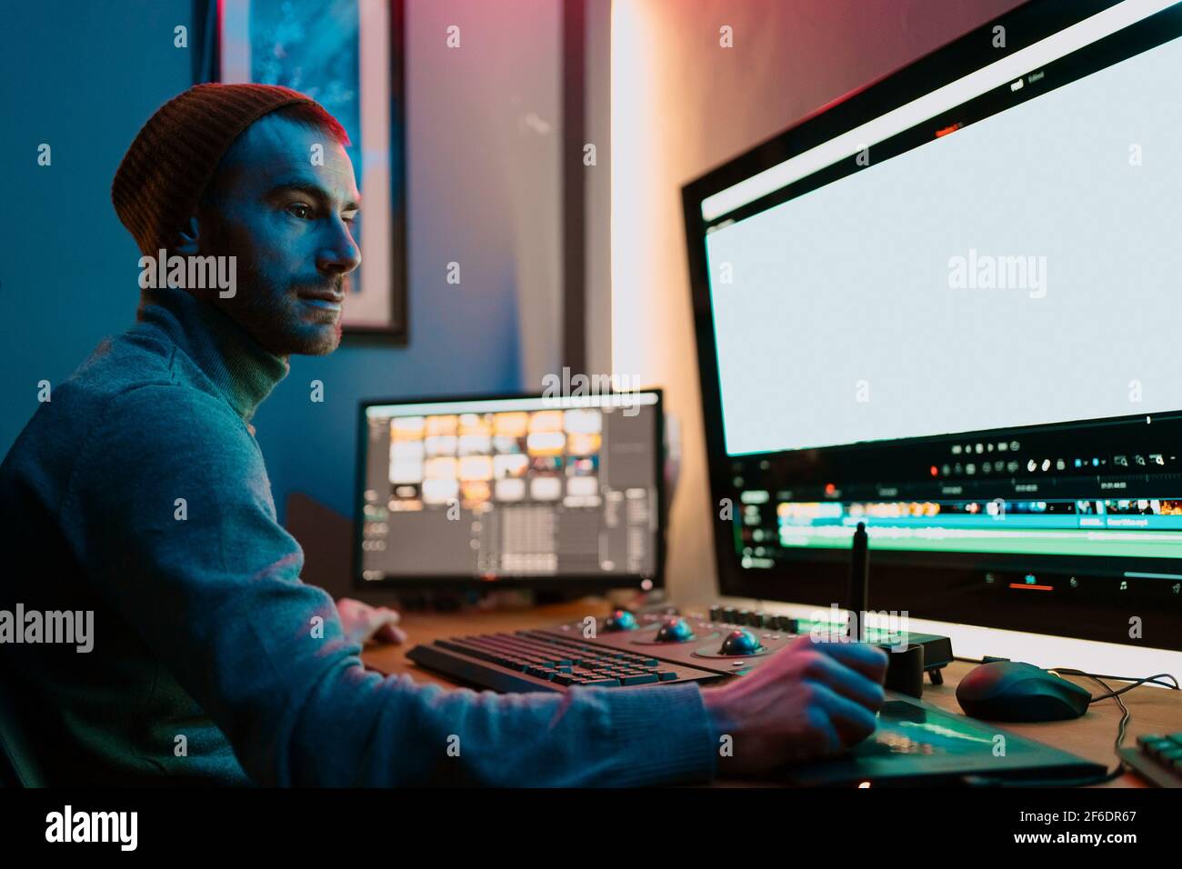 Attractive Male Video Editor Works with Footage or Video on His Personal Computer, he Works in Creative Office Studio or home. Neon lights Stock Photo