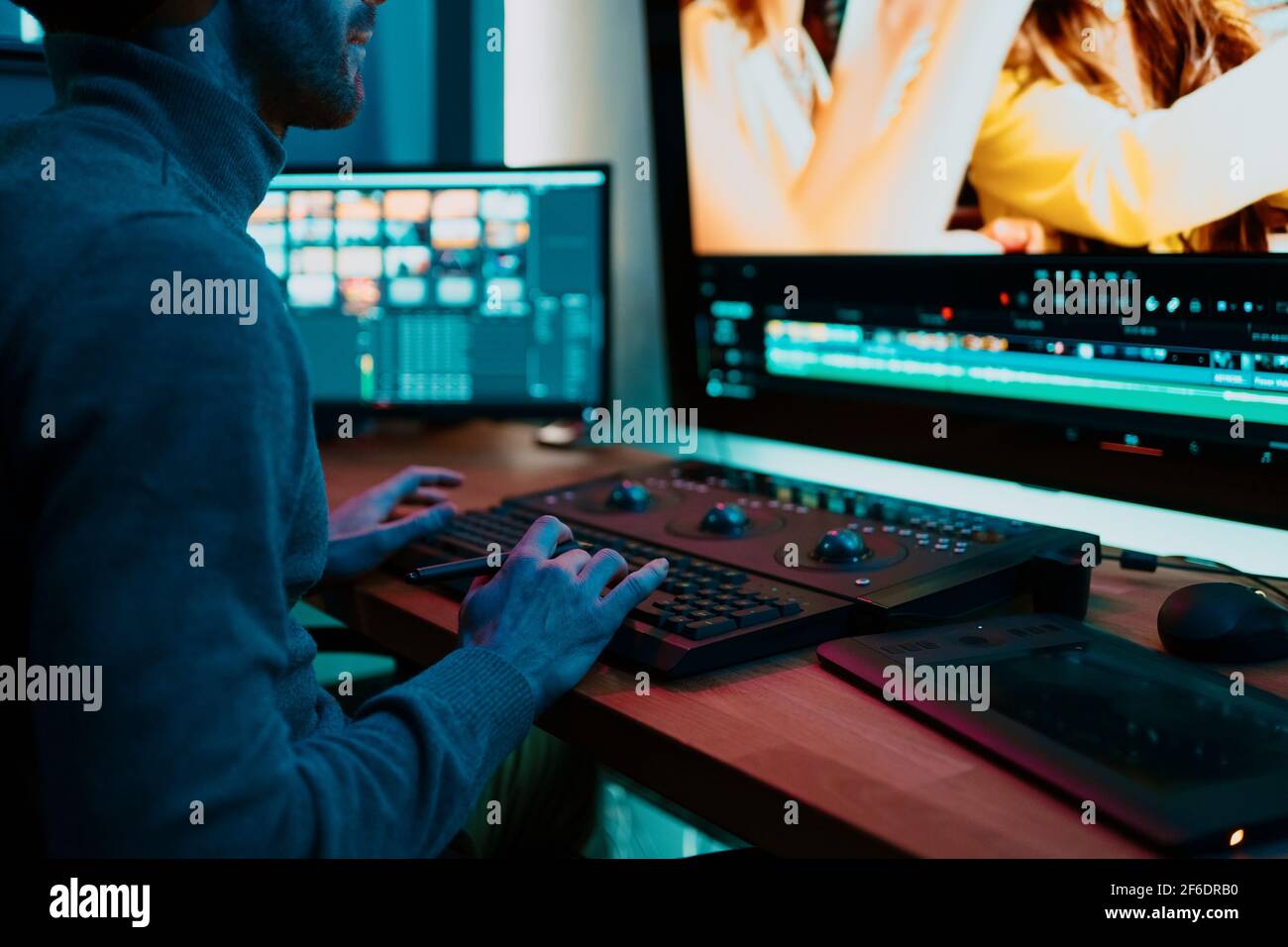 Attractive Male Video Editor Works with Footage or Video on His Personal Computer, he Works in Creative Office Studio or home. Neon lights Stock Photo