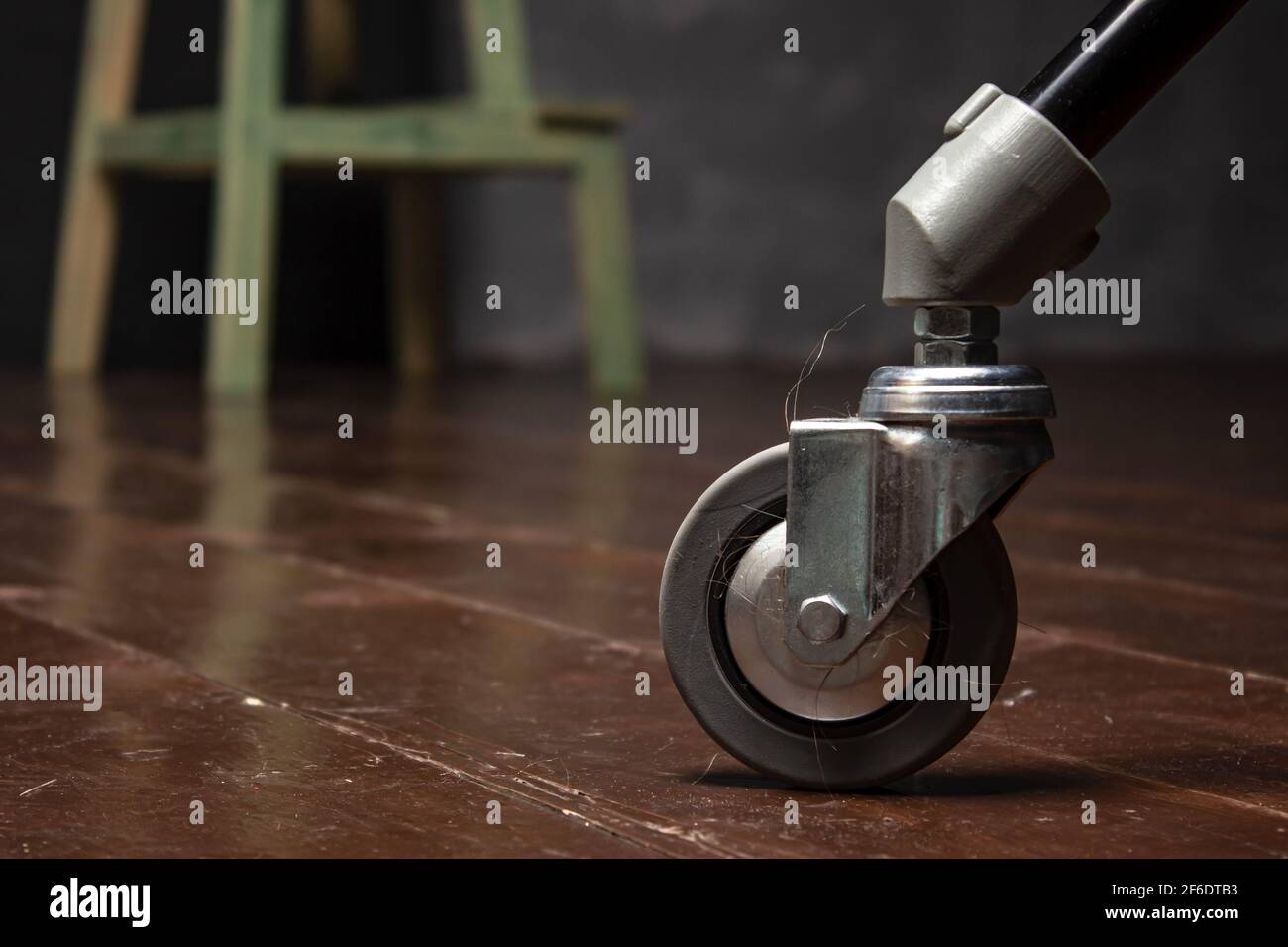 Ride on a chair leg with tangled hair on the wooden floor. Dirt stuck to the wheel. Close-up. Stock Photo