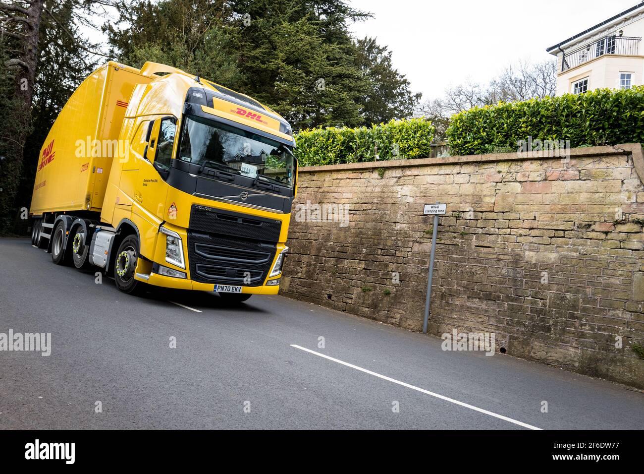 Volvo FH heavy truck in DHL livery colour yellow drives along a narrow country lane. Stock Photo
