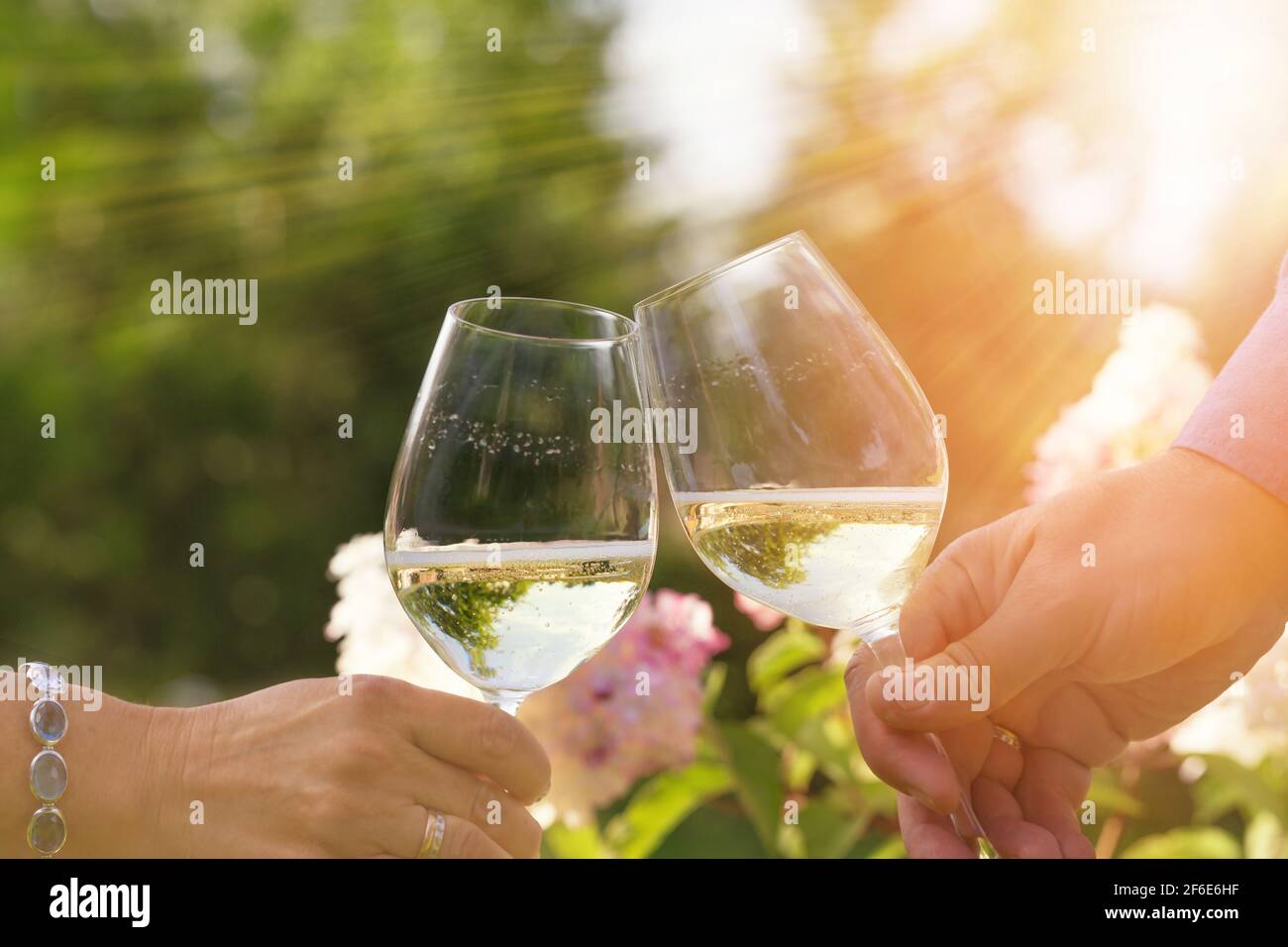Couple romantically celebrate outdoors with glasses of white wine, proclaim toast People having dinner in a home garden in summer sunlight. Stock Photo