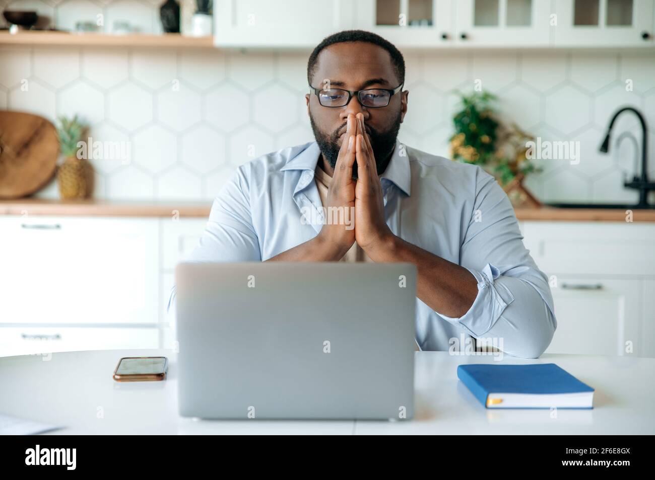 Concentrated business african american man working from home, sitting at work desk, using laptop, looking at laptop thoughtfully, hands near face, thinking about financial business plan or new startup Stock Photo