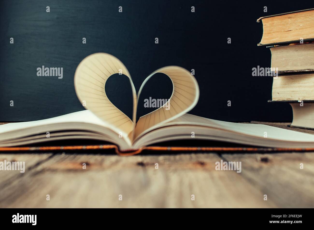 Sheets of a notebook in a cage wrapped in the shape of a heart.In the background is a stack of books and a black board.Education concept.Valentine's D Stock Photo