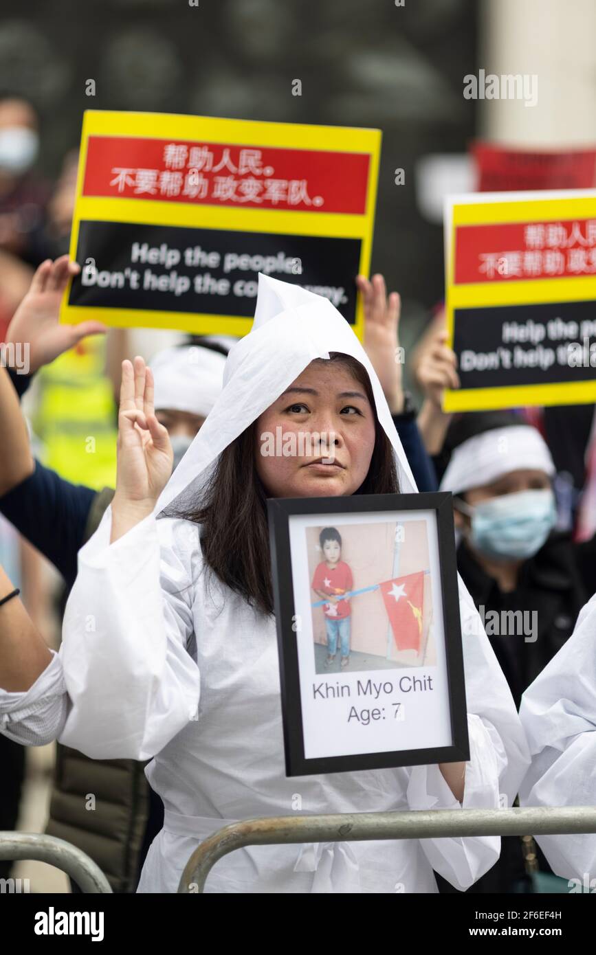 London, UK. 31st Mar, 2021. A female protester dressed in white makes the three finger salute of resistance and holds a photograph of a deceased victim outside the Chinese Embassy. Protesters gathered in Parliament Square - wearing face masks and observing social-distancing - before marching to the Chinese Embassy in solidarity with the people of Myanmar against the military coup and state killings of civilians. Speeches were given outside the embassy. Since the beginning of the military coup on the 1st of February over 520 people have been killed in Myanmar by security forces. Last Saturday w Stock Photo