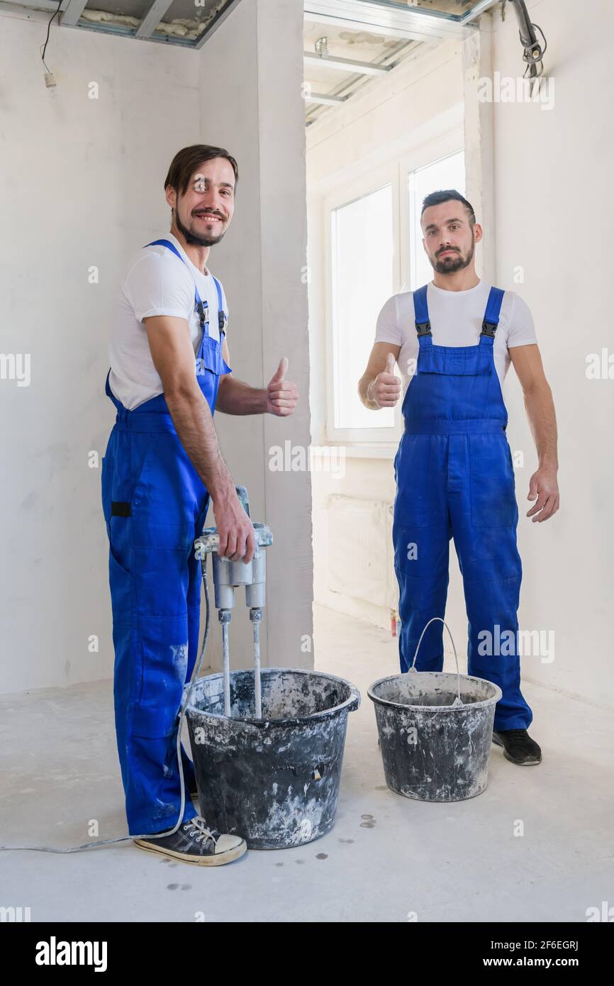 Two construction workers in blue uniform prepare cement in a bucket Stock Photo