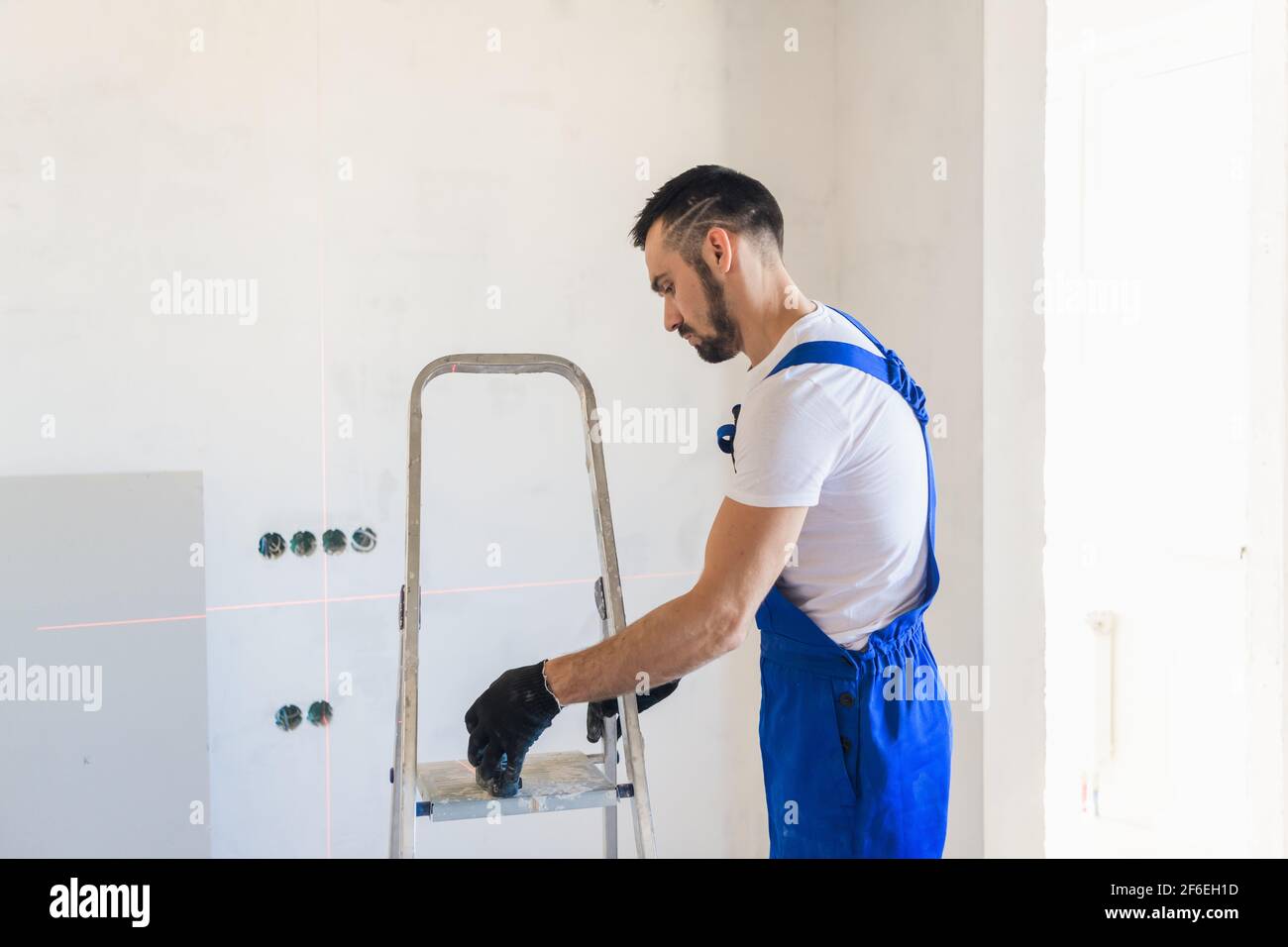 A builder in overalls marks the wall using a laser level Stock Photo