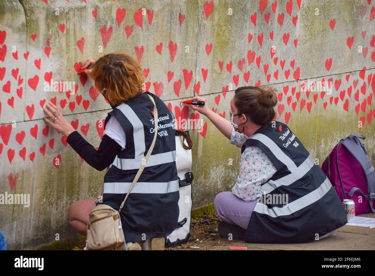 London, United Kingdom. 31st March 2021. Volunteers paint red hearts on the National Covid Memorial Wall. Nearly 150,000 hearts will be painted by volunteers, one for each Covid-19 victim in the UK to date, on the wall outside St Thomas' Hospital opposite Houses Of Parliament. Stock Photo