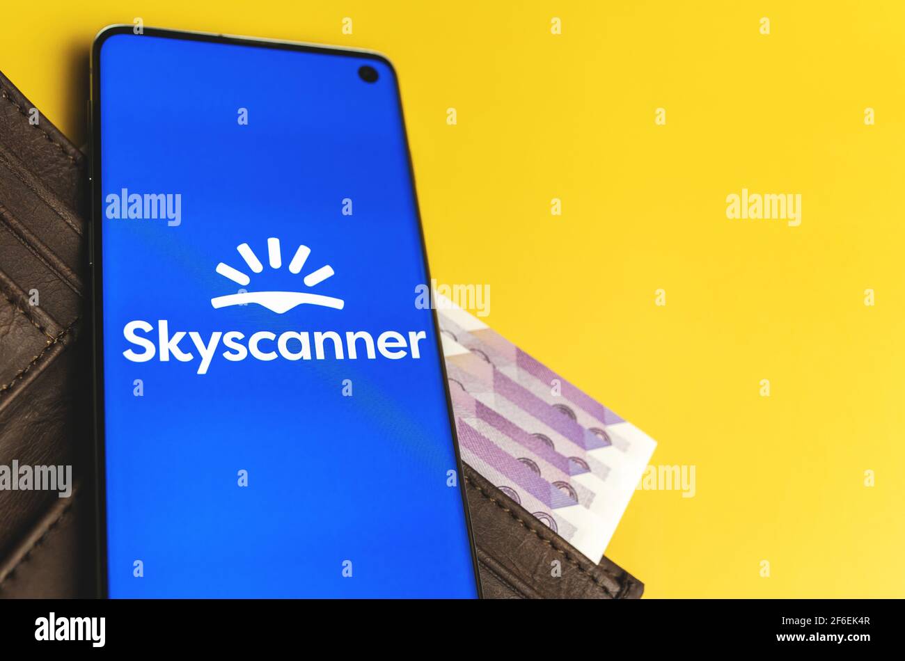 SWANSEA, UK - MARCH 28, 2021: Scyscanner app logo displayed on smartphone laying on brown wallet with money on yellow background Stock Photo