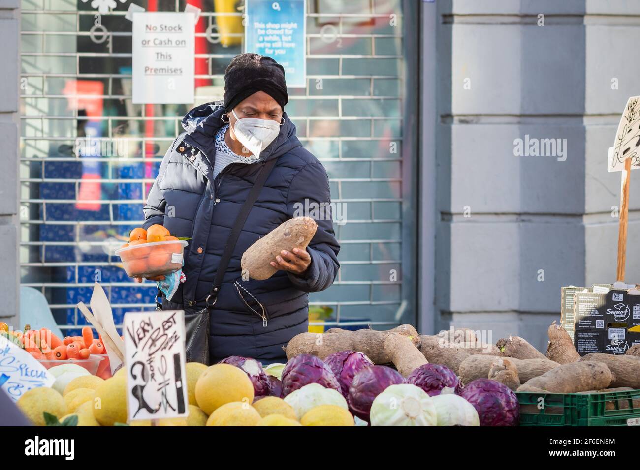 London, UK - 5 February, 2021 - A black woman wearing a protective face mask while shopping at an outdoor produce stall on Wood Green high street Stock Photo