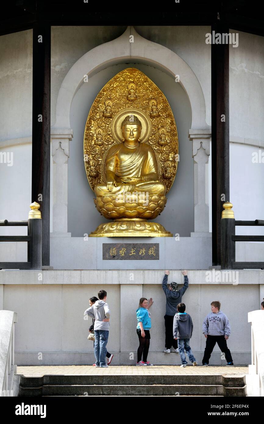 Kids hanging with the Buddha. A gilded bronze sculpture of the Buddha at the Peace Pagoda, Battersea Park, London. Stock Photo