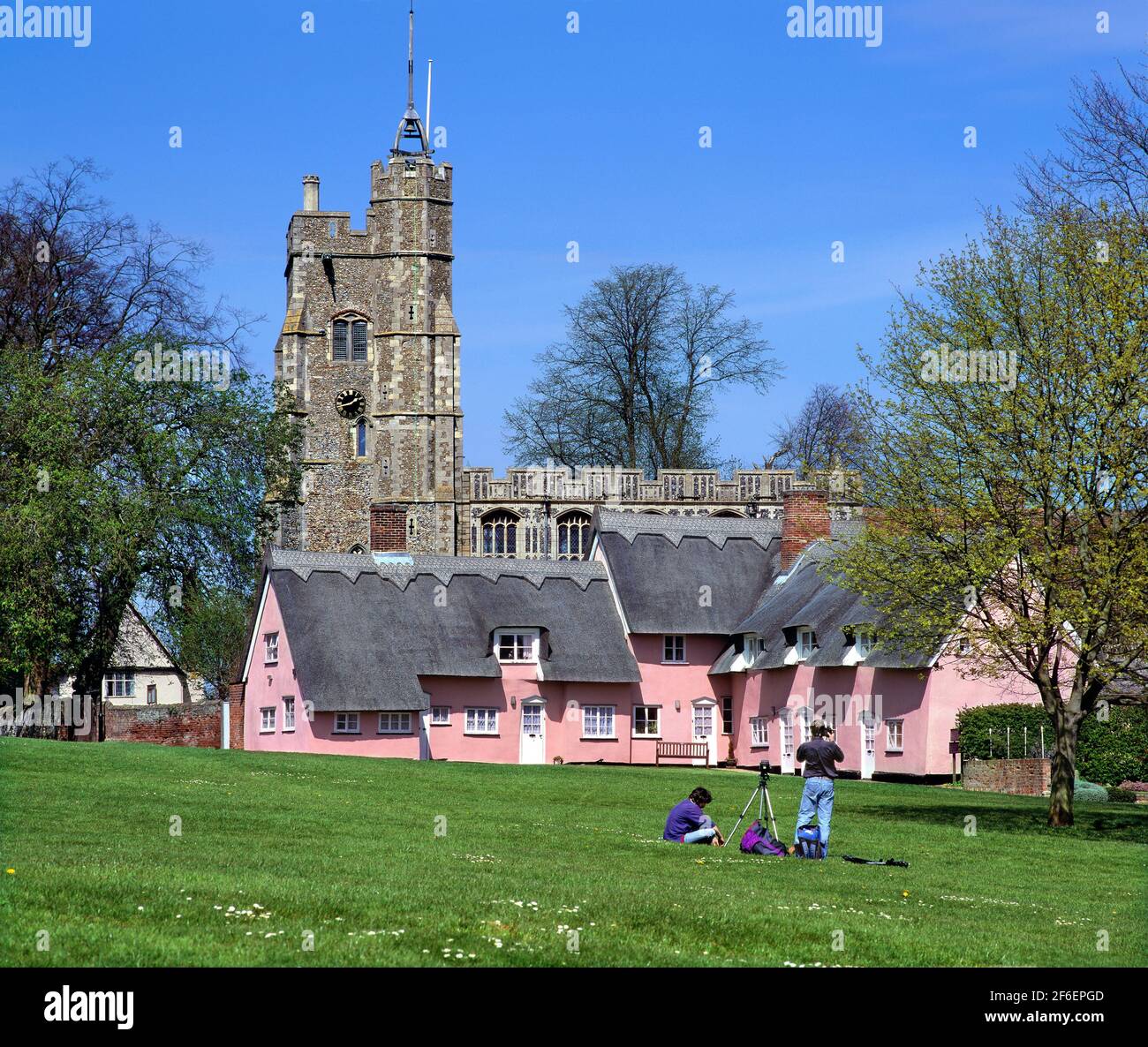 A photographer taking photographs of colour-washed thatched cottages and the Church of St. Mary, by the village green in Cavendish, Suffolk. Stock Photo