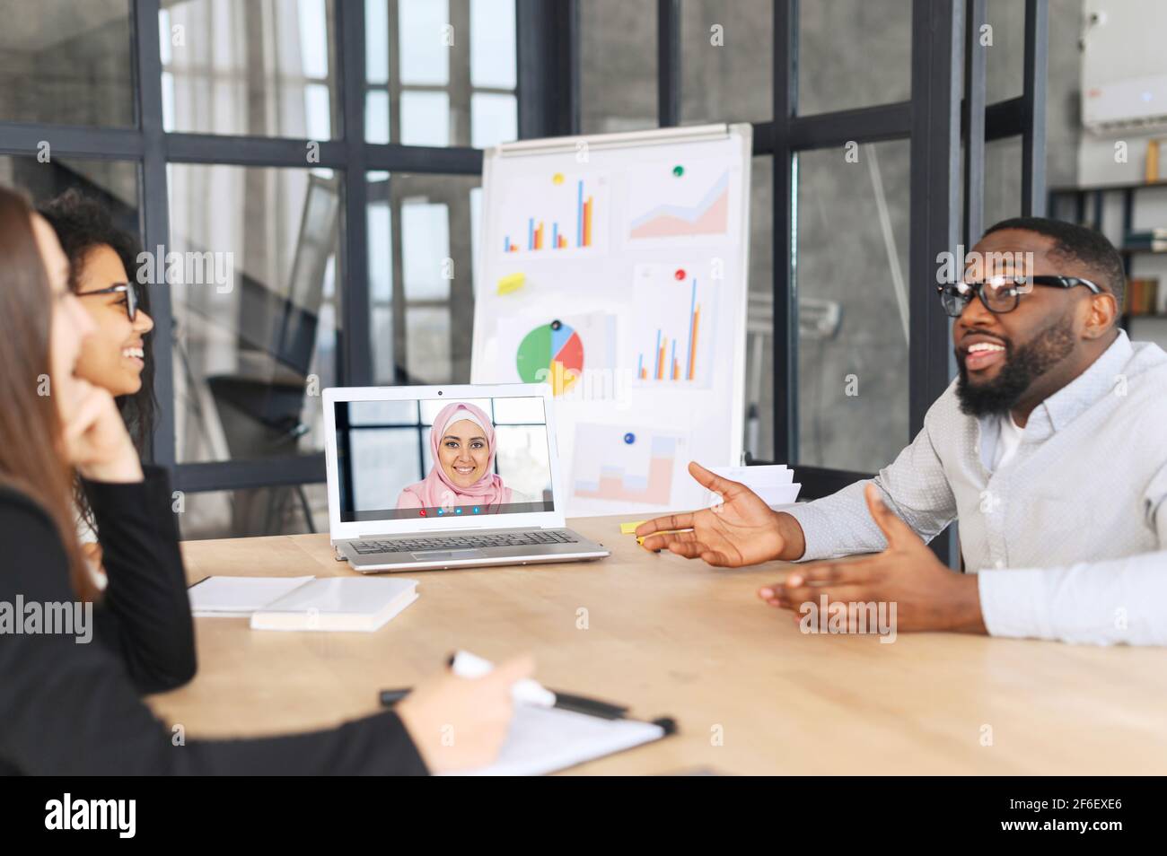 Diverse work team using app on the laptop for connect with female arab colleague on the screen. Group of hr employees interviewing female muslim job seeker on the distance. Video conference Stock Photo