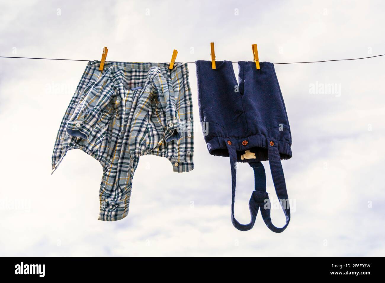 Elegant baby trousers and shirt pinned with wooden pegs against cloudy sky Stock Photo