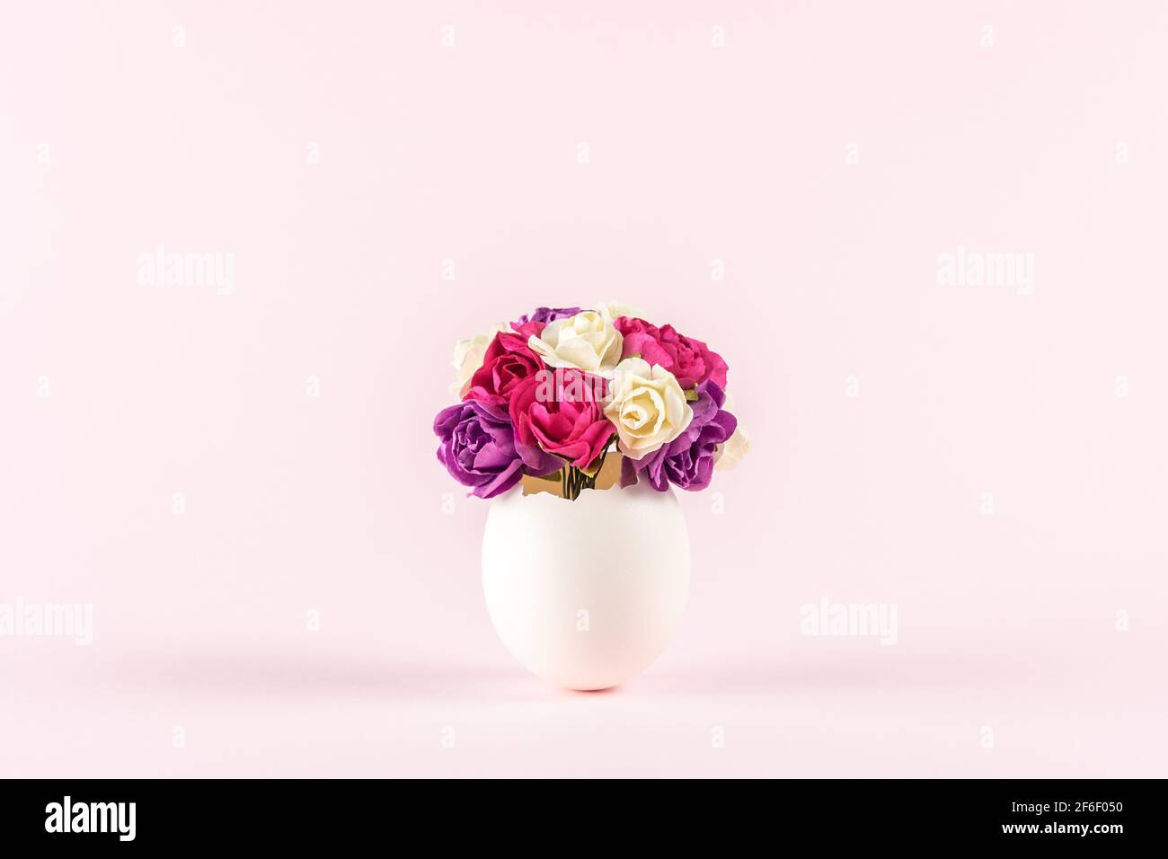 Spring flowers in cracked eggshell against pastel pink background. Easter minimal concept. Creative Happy Easter or spring layout. Stock Photo