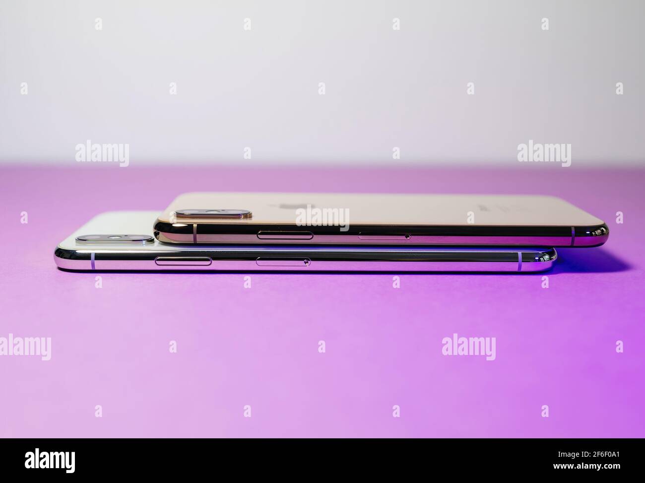Side view of two latest Apple Computers iPhone XS gold color 256 GB smartphones Max and smaller versions - gold and silver colors - magenta background Stock Photo