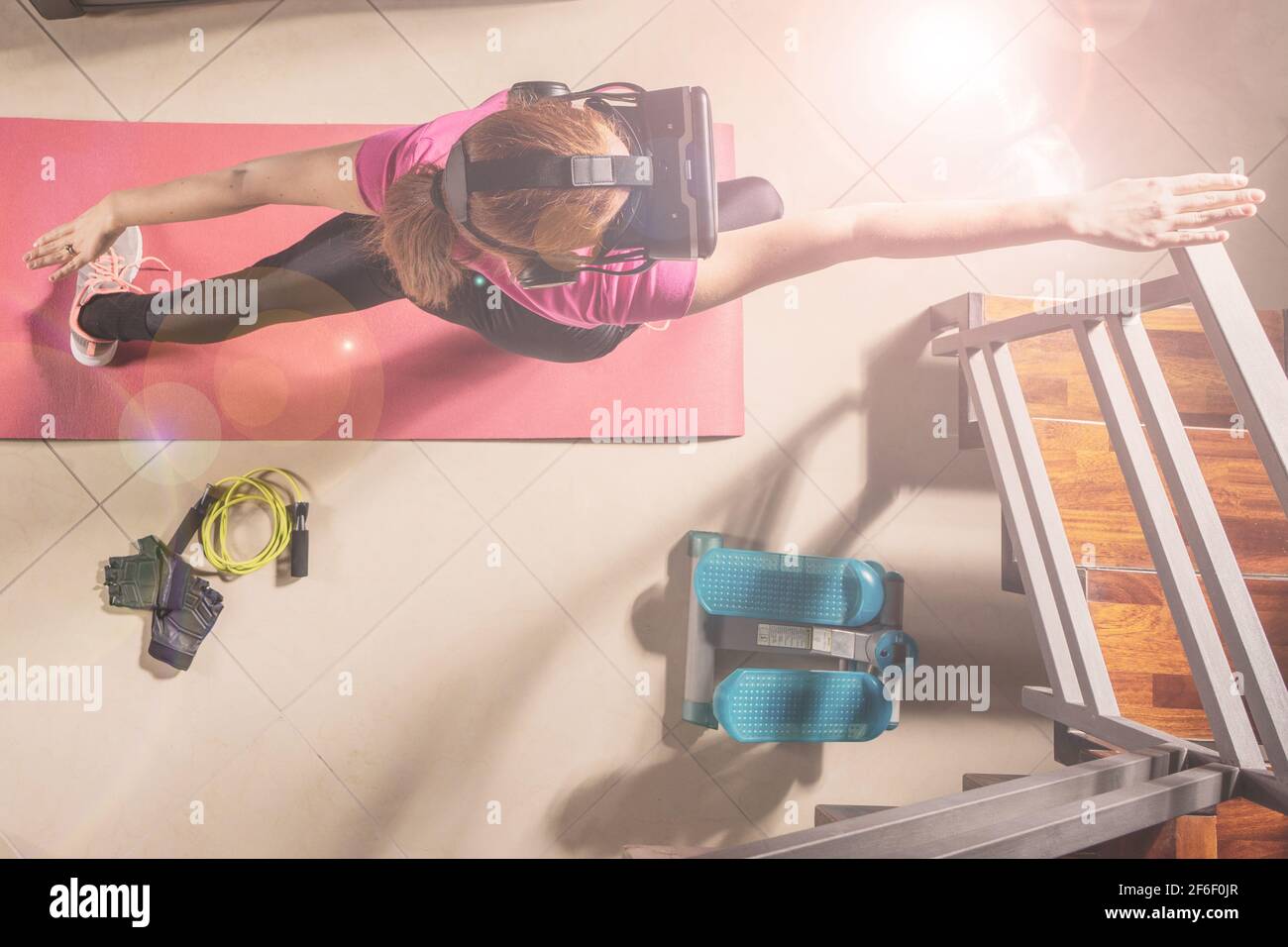 Attractive red hair sportswoman training in her beautiful house doing stretching with vr futuristic goggles - Ginger athletic model exercising Stock Photo