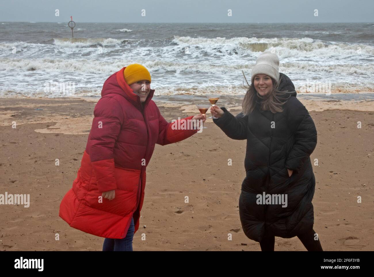 Portobello, Edinburgh, Scotland, UK weather. 31st March 2021. Stormy afternoon with temperature 6 degrees centigrade and rough seas on the Firth of Forth for Robyn (red Coat) who is celebrating her 39th Birthday today on the beach with her best friend Emma. They would normally be in a restaurant but not currently possible due to Covid -19 restrictions. Stock Photo