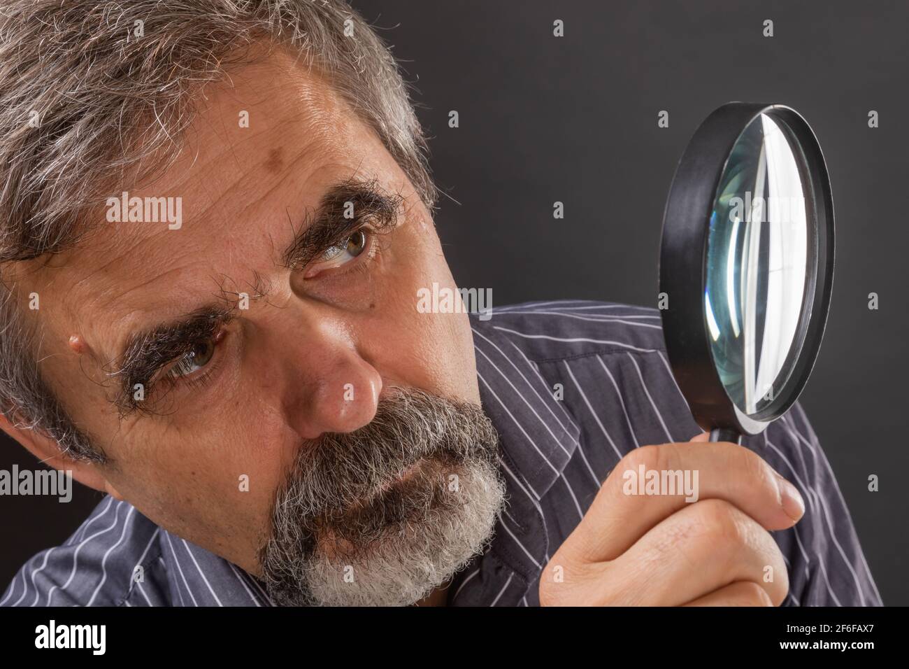 Elderly gray-haired man with a beard carefully examine something through a magnifying glass Stock Photo