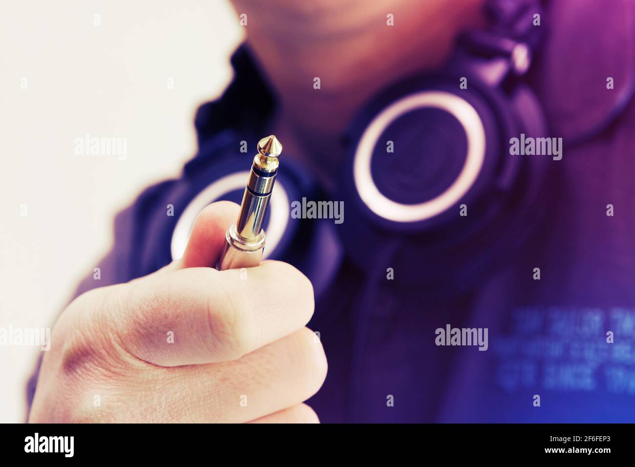 Close-up of stereo jack, TRS connector, held by man with headphones around his neck. DJ, music, connectivity concepts Stock Photo