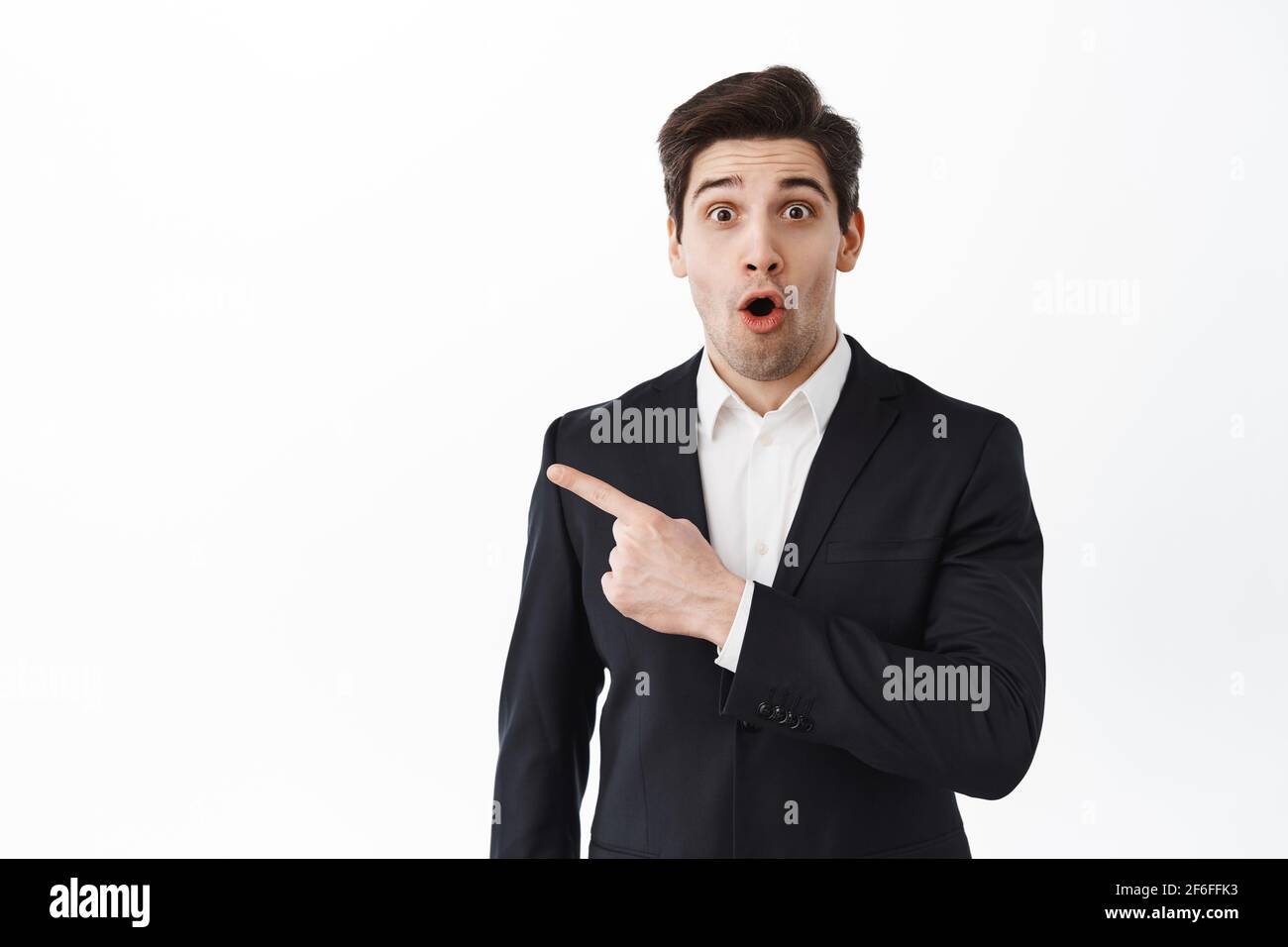Surprised real estate agent, entrepreneur corporate man make wow face, look intrigued and amazed, pointing aside at logo, show banner, standing over Stock Photo