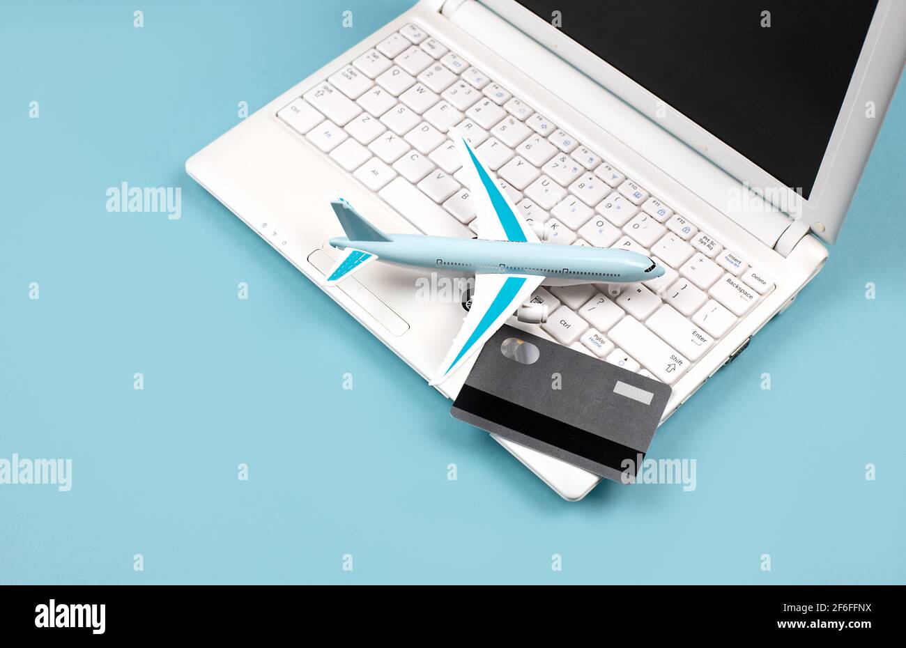 White laptop on a blue background. Nearby is a bank card and a miniature airplane. Concept - Online booking of air tickets, travel planning. Stock Photo